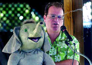 Ventriloquist Joe Gandelman shoots a stream of water toward the audience from the trunk of 